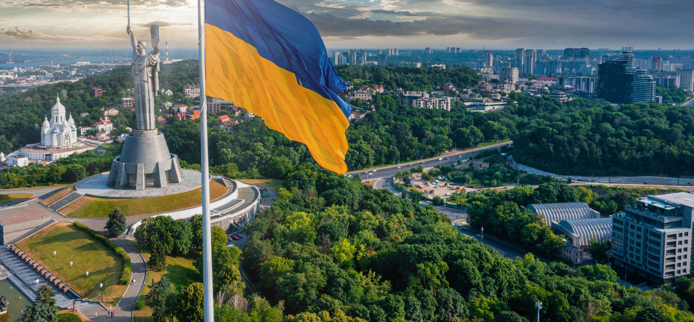 Image: Ukrainian flag waving in the wind against the city of Kyiv, Ukraine (Photo Credit: Adobe Stock/ingusk)