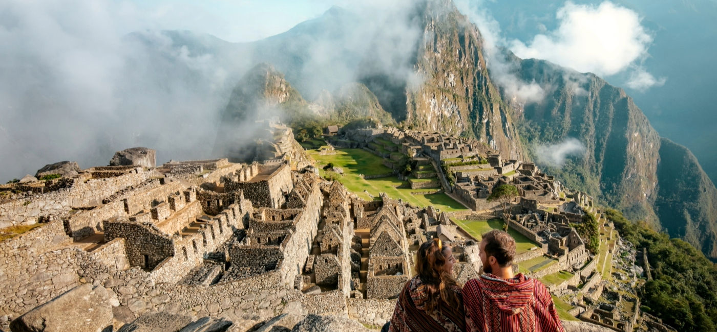 Image: A couple sits overlooking the ruins of Machu Picchu. (Photo Credit: marina / AdobeStock)