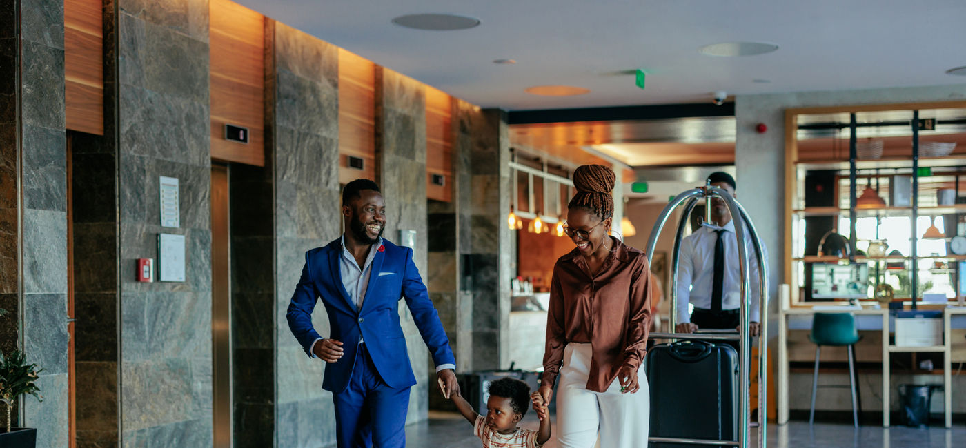 Image: An African American family walking through the lobby of luxury hotel (Photo Credit: Dimensions / Getty Images)