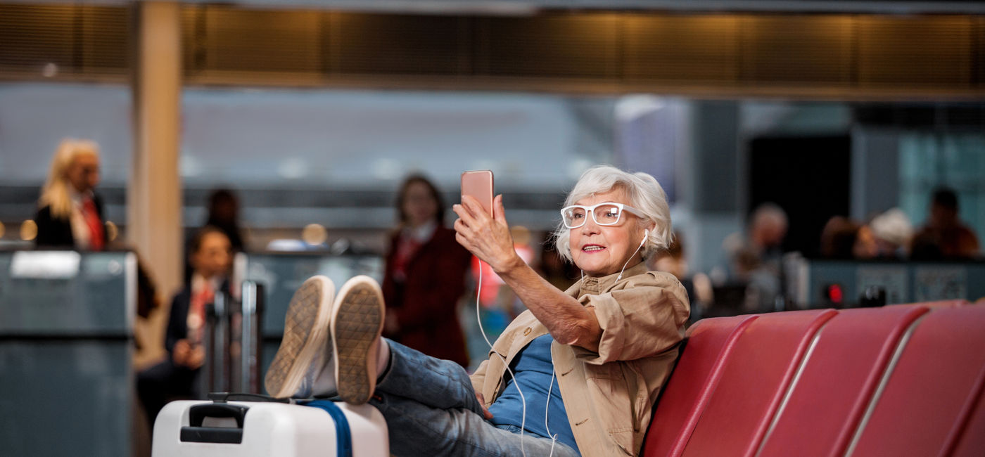 Image: Elderly woman takes a selfie at the airport  (Photo Credit: Yakobchuk Olena / Adobe Stock)