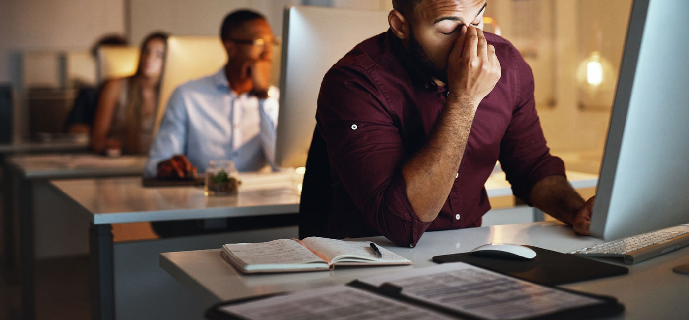 Image: Burnt-out office worker in front of his laptop. (Photo Credit: Adobe Stock/Jadon B/peopleimages.com)