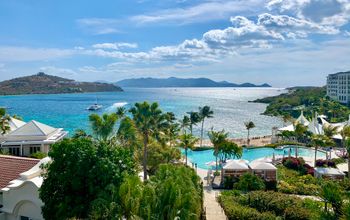 Hotel overview with pool, beach, and sun-drenched ocean with island visible across ocean channel