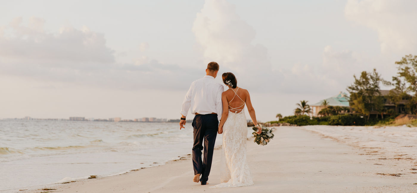 Image: Newlywed couple walking down the beach. (Photo Credit: Adobe/MeganMahoneyPhotos)