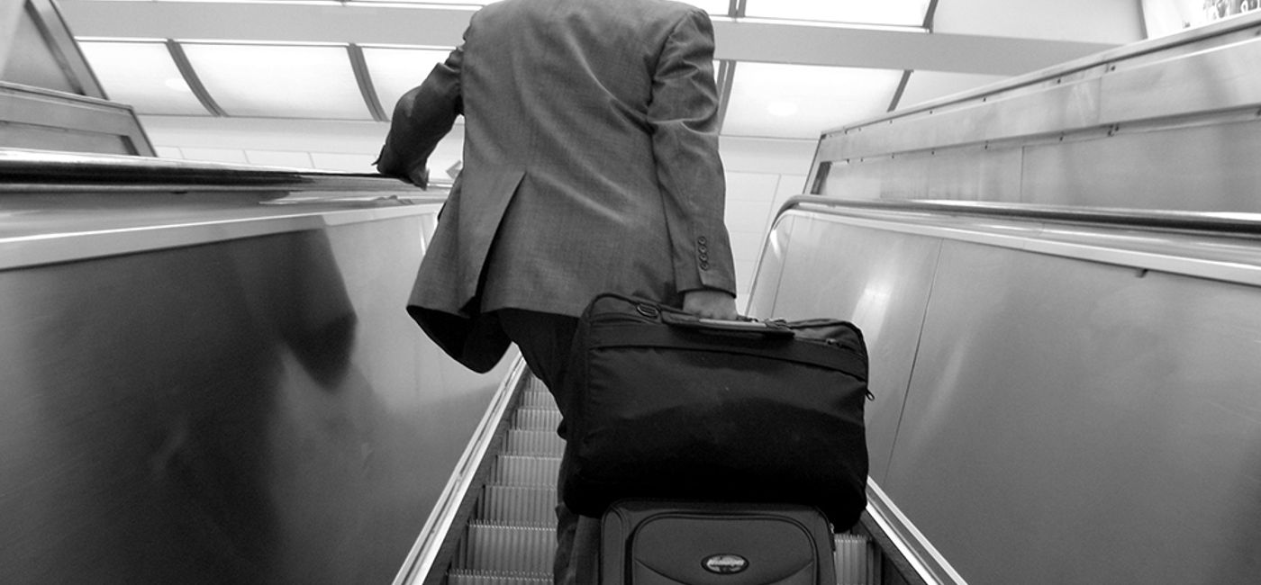 Image: PHOTO: Business traveler lugging a suitcase up an escalator at an airport. (photo via Flickr/frankieleon)