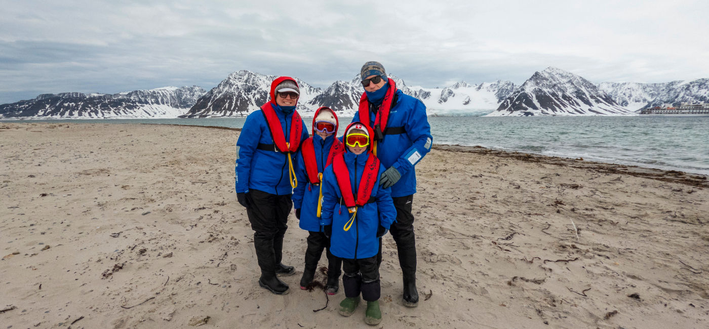 Image: A family takes a photo with the Greg Mortimer in the background in Smeerenburg, Svalbard. (Photo Credit: Aurora Expeditions)