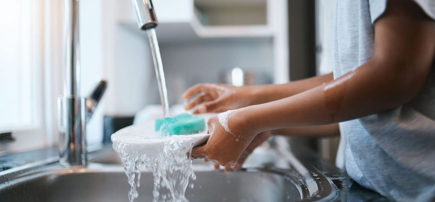 Image: Woman cleaning dishes. (Photo Credit: Adobe/Wesley JvR/peopleimages.com)
