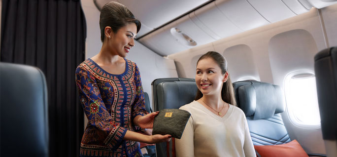 Eine Flugbegleiterin von Singapore Airlines überreicht einem Premium-Economy-Class-Reisenden ein neues „Out of the Woods“-Ausstattungsset. Singapore Airlines, Premium Economy, SIA, Flugausstattungsset