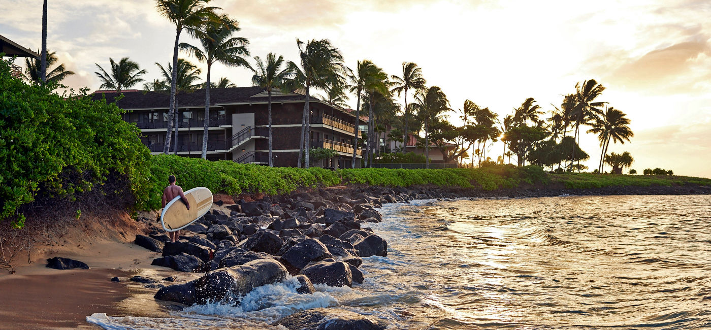 Image: A paddleboarder walks along the beach at Ko'a Kea Resort on Po'ipu Beach. (Photo Credit: The Meritage Collection)