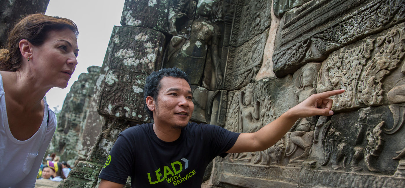 Image: A G Adventures CEO explains carvings to a traveler at Angkor Wat. (Photo Credit: G Adventures)