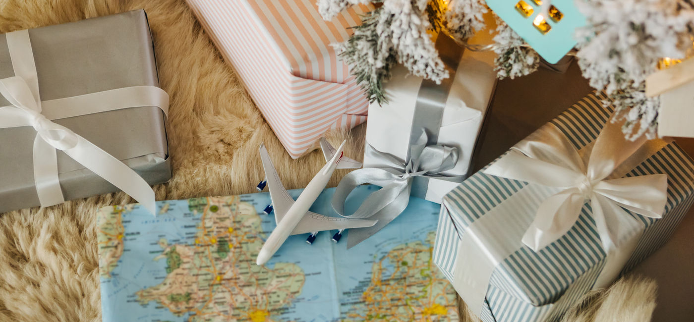 Image: Toy airplane sitting on a map surrounded by holiday gifts. (Photo Credit: Adobe Stock/Iryna&Maya)