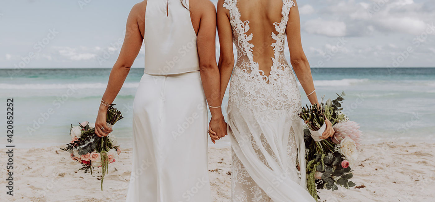 Image: LGBTQ+ couple getting married on the beach. (Photo Credit: Martincorr/Adobe Stock)