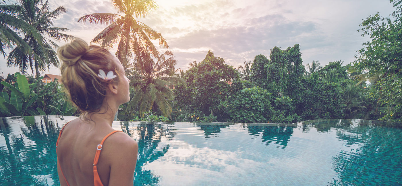 Image: Woman by the edge of an infinity pool enjoying tropical climate in Ubud, Bali. (photo via iStock/Getty Images E+/swissmediavision)