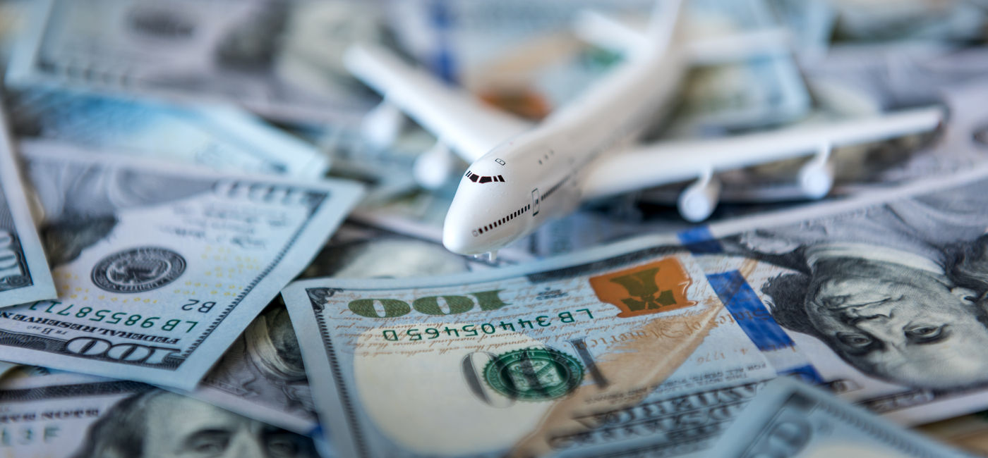 Image: A toy airplane sitting atop a pile of US cash. (Photo Credit: Ivan Kmit / Adobe Stock)