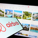 Airbnb logo displayed on a smartphone in front of a listings webpage. 