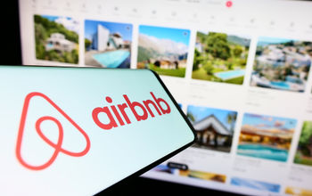 Airbnb logo displayed on a smartphone in front of a listings webpage.