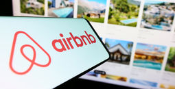 Airbnb logo displayed on a smartphone in front of a listings webpage.