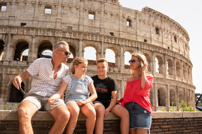A family of travelers sits in front of the Colosseum in Rome, Italy.
