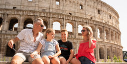 A family of travelers sits in front of the Colosseum in Rome, Italy.