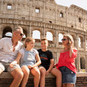 A family of travelers sits in front of the Colosseum in Rome, Italy.