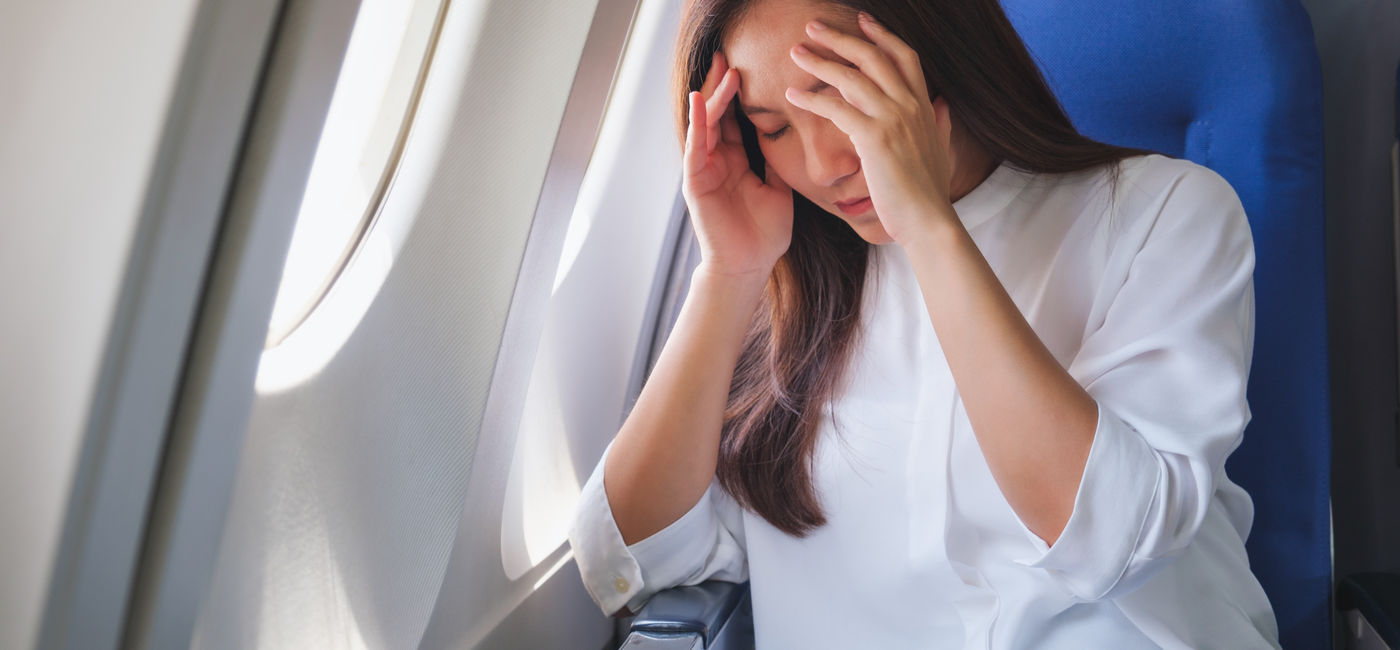 Image: Woman flying on a plane while dealing with headache pain. (Photo Credit: Adobe Stock/Farknot Architect)