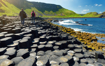 Two tourists walking at Giants Causeway, an area of hexagonal basalt stones, County Antrim, Northern Ireland Famous tourist attraction
