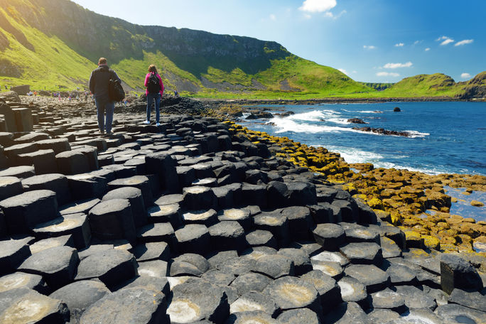 Two tourists walking at Giants Causeway, an area of hexagonal basalt stones, County Antrim, Northern Ireland Famous tourist attraction Two tourists walking at Giants Causeway, an area of hexagonal basalt stones, County Antrim, Northern Ireland Famous tourist attraction
