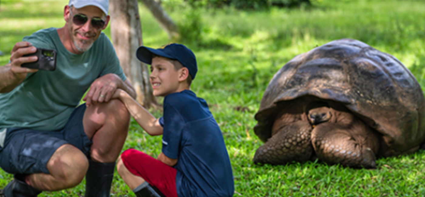 Image: Family taking a picture with a giant tortoise (Photo Credit: National Geographic-Lindblad Expeditions)