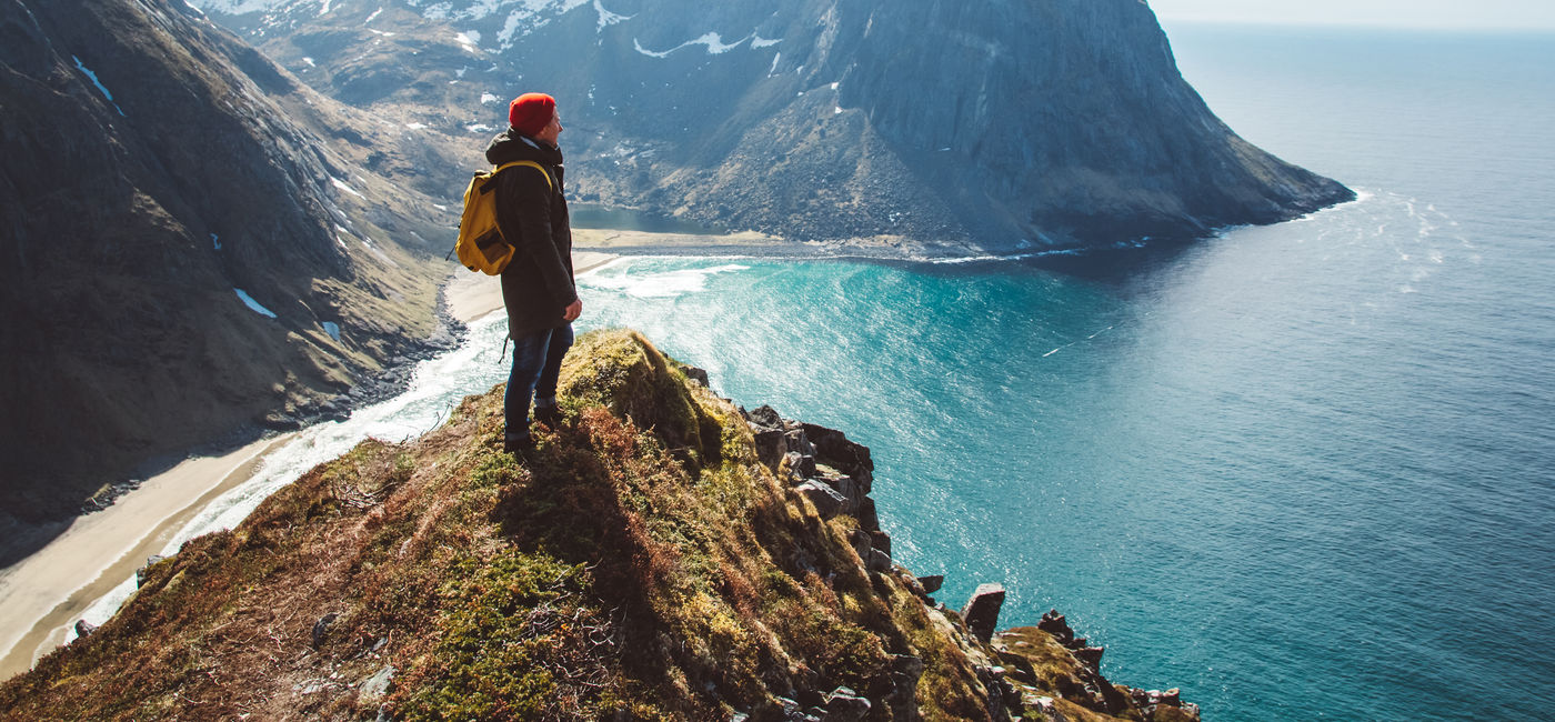 Image: Backpacker standing on top of a mountain overlooking the sea. (Photo Credit: Adobe Stock/Andriy)