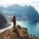 Backpacker standing on top of a mountain overlooking the sea.
