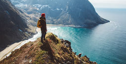 Backpacker standing on top of a mountain overlooking the sea.
