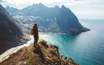 Backpacker standing on top of a mountain overlooking the sea.