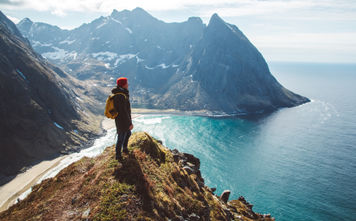 Backpacker standing on top of a mountain overlooking the sea.
