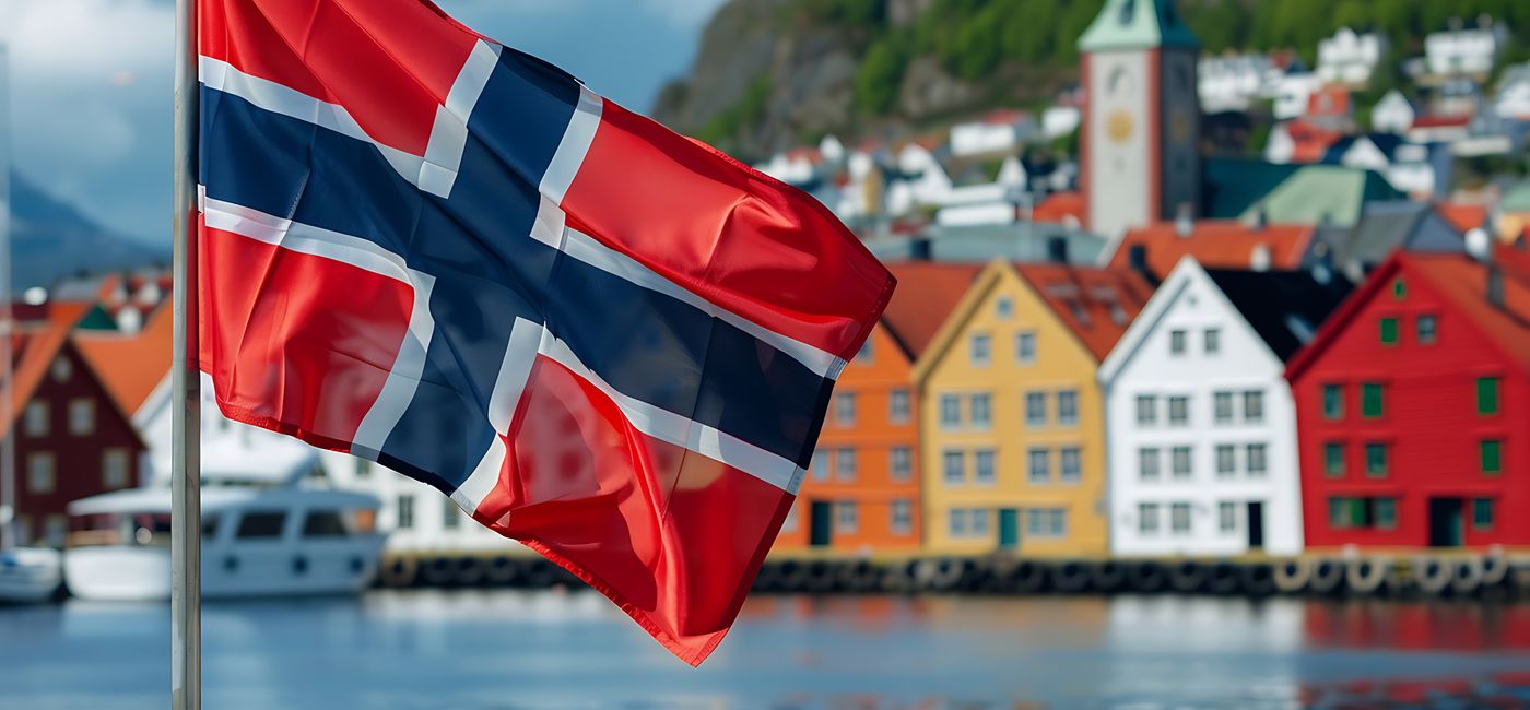 Image: Norwegian national flag in front of colorful houses in Bergen, Norway. (Photo Credit: Adobe Stock/Mahmud Creative)