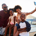 Family posing for selfie next to car packed for road trip.