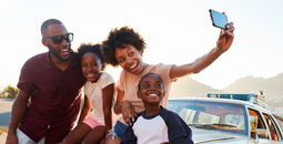 Family posing for selfie next to car packed for road trip.