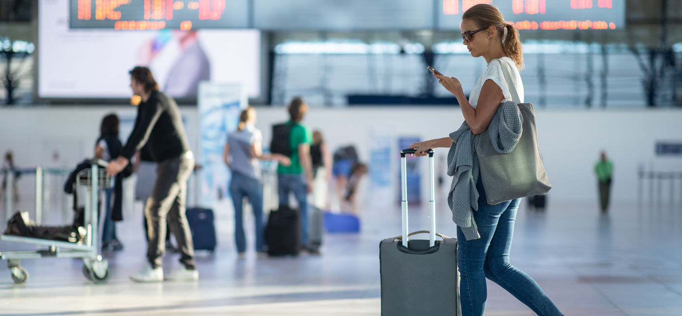 Image: Woman walking into an airport on her smartphone. (Photo Credit: Adobe/lightpoet)