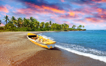 Wooden fishing boat on beach at sunset in Jamaica.