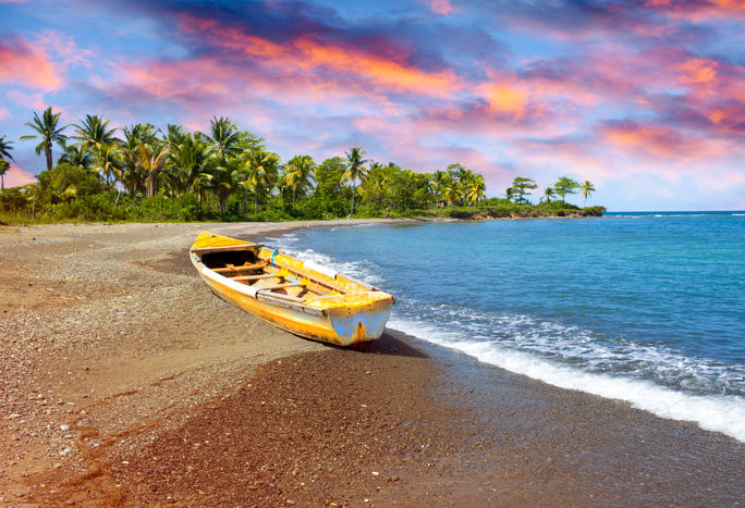 Wooden fishing boat on beach at sunset in Jamaica.