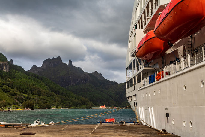 A cruise ship tied up at a wharf with mountain peaks in the background