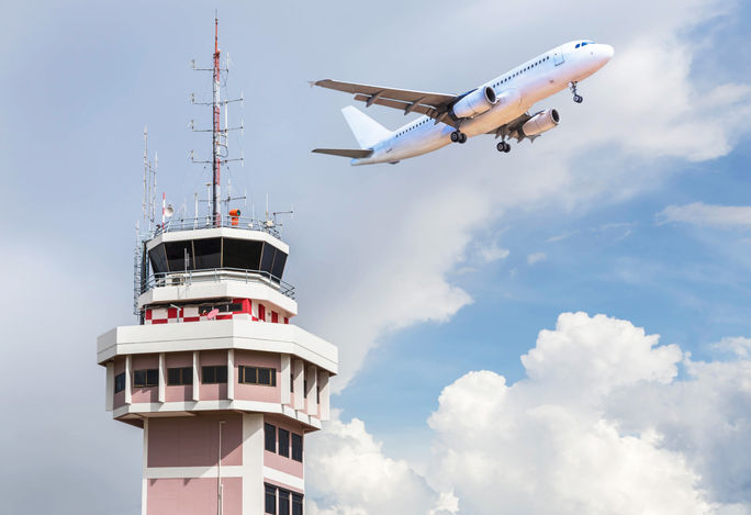 Air traffic control tower with an airplane taking off in the foreground. 