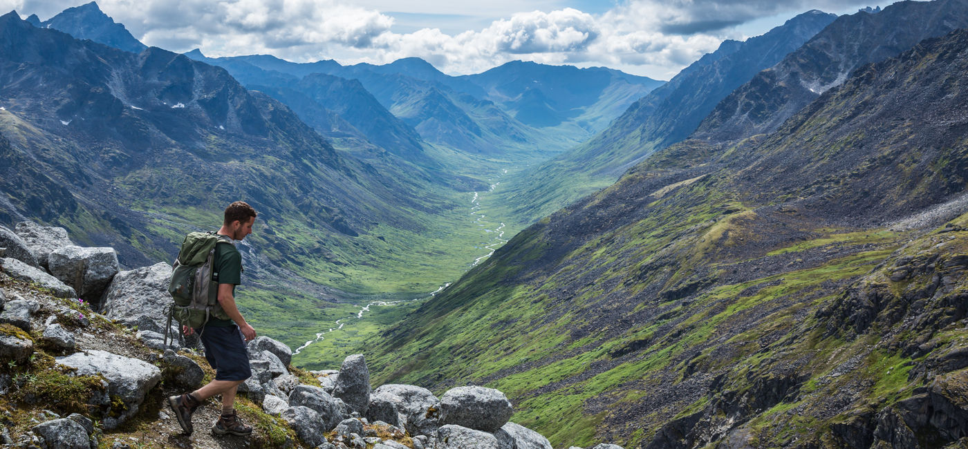Image: Hiker making his way down a steep trail in Alaska's Talkeetna Mountains. (Photo Credit: Adobe Stock/DCrane Photography)
