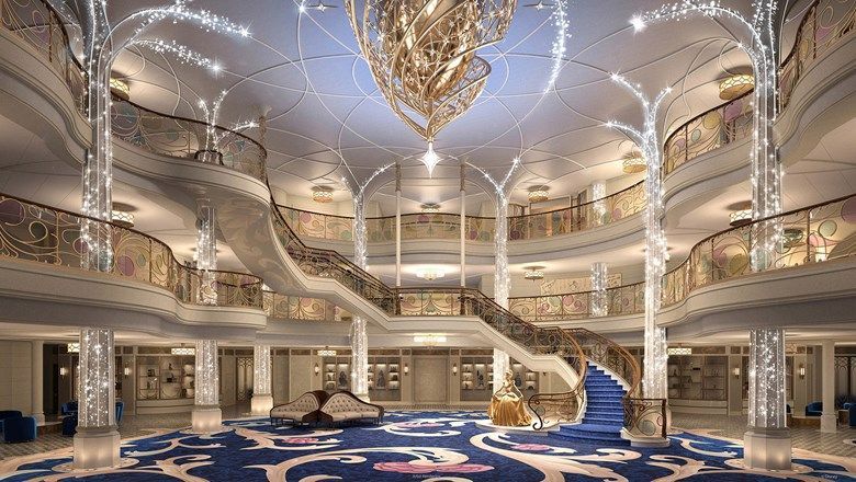 The Grand Hall onboard the Disney Wish, complete with a “wishing star” chandelier, and a bronze statue of Cinderella, along with a theatrical stage below.