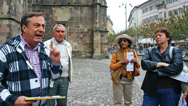 An animated local tour guide in Bolzano, Italy, with a Trafalgar tour director looking on. An animated local tour guide in Bolzano, Italy, with a Trafalgar tour director looking on.