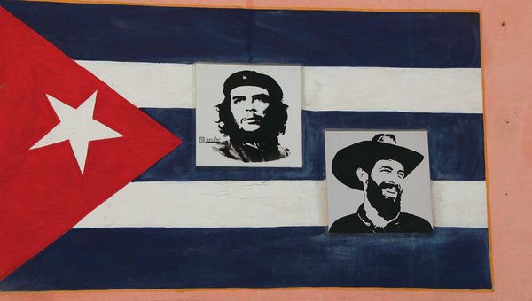 A flag in Cuba carries stylized visages of revolutionaries Che Guevara and Camilo Cienfuegos. A flag in Cuba carries stylized visages of revolutionaries Che Guevara and Camilo Cienfuegos.