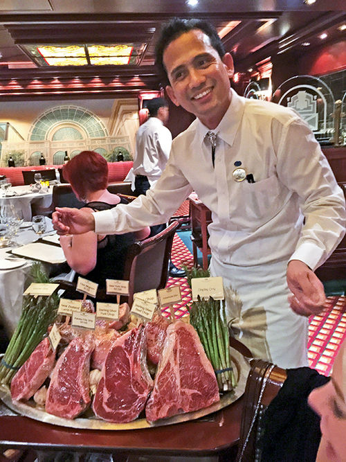 A waiter in the Crown Grill specialty restaurant displays steaks that can be ordered.