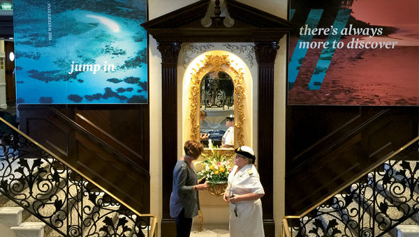 Two Fathom crew members on an Adonia staircase. The original classical decor is flanked by two Fathom photo panels. Two Fathom crew members on an Adonia staircase. The original classical decor is flanked by two Fathom photo panels.