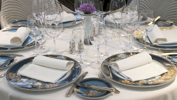 Tables at Compass Rose, the Navigator’s main dining room, are set with Versace chargers and plates. Tables at Compass Rose, the Navigator’s main dining room, are set with Versace chargers and plates.