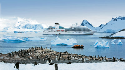 A zodiac boat with passengers from the Seabourn Quest heads for a beach full of penguins in Antarctica.
