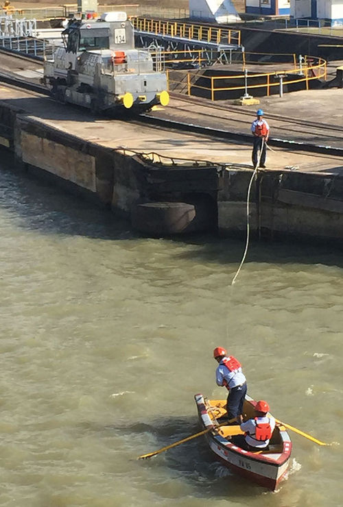 Workers use a rowboat to deliver a towline to ships going through the locks. The lines are attached to the mule in the background. Workers use a rowboat to deliver a towline to ships going through the locks. The lines are attached to the mule in the background.