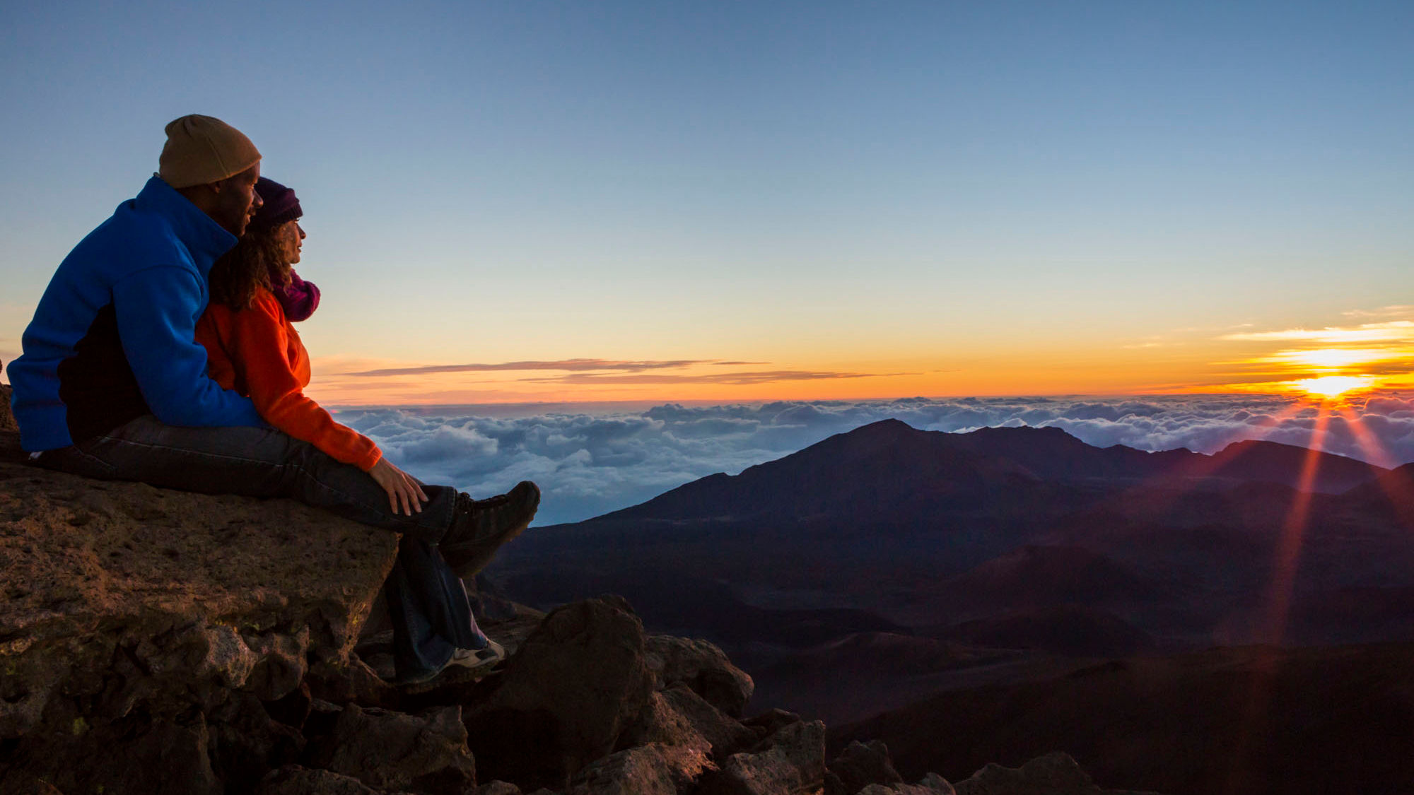 A couple takes in a sunrise from the Haleakala National Park summit area.